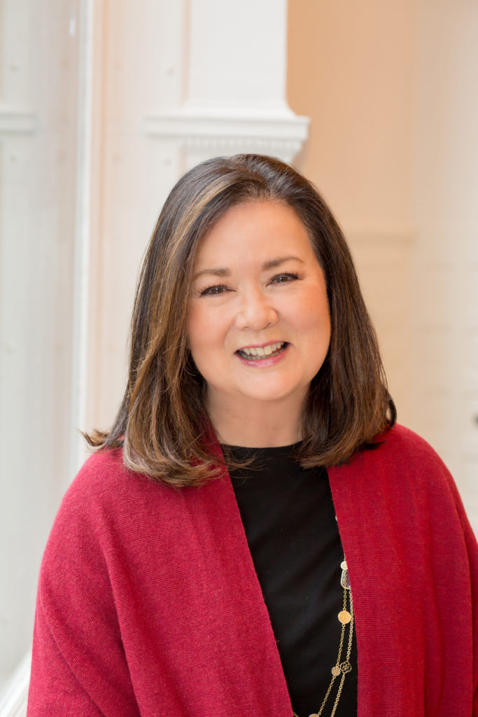 Smiling professional in a red cardigan photographed indoors in natural window light